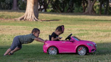 a kid pushing a car with a another kid sitting in it