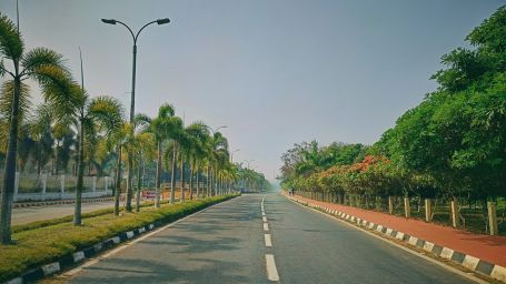 an empty road in Agartala with trees on either side and street light as a divider