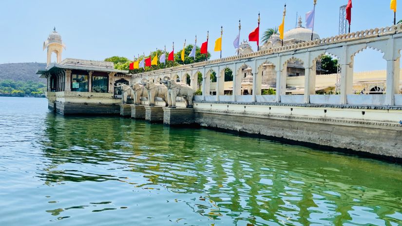 Pier with colorful flags by the green lake - Jag Mandir with blue sky in the background