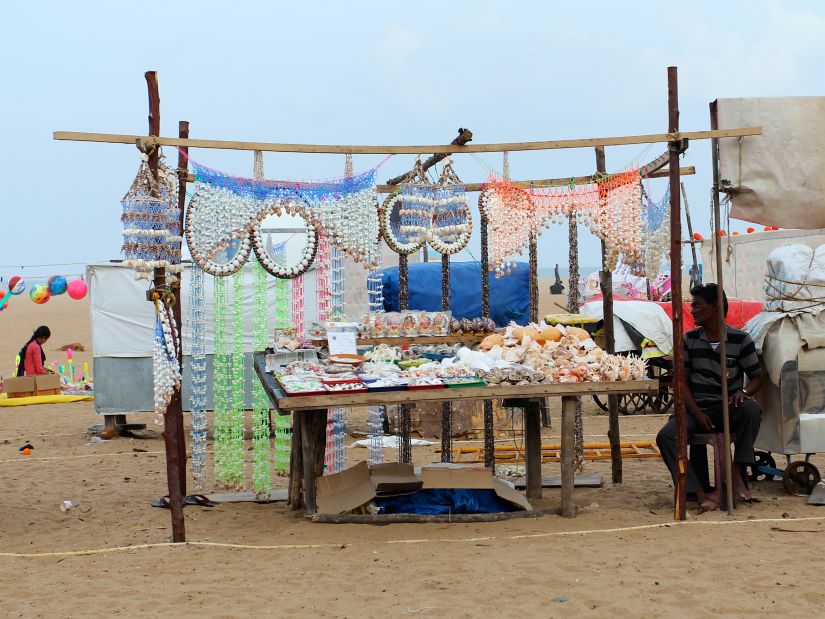 a street market on the beach with a person sitting next to a stand