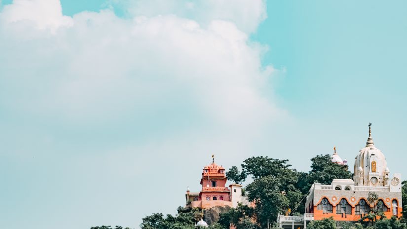 A hilltop temple with domes and spires, brightly colored against a cloudy sky.