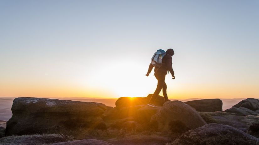 a person walking on rocks during his trek with the sun setting in the background