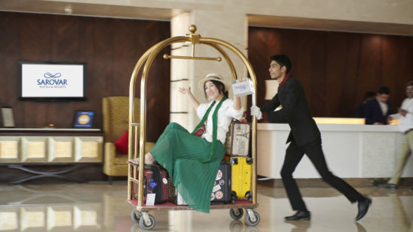 a bell boy pushing a bell trolley with a woman on top of it