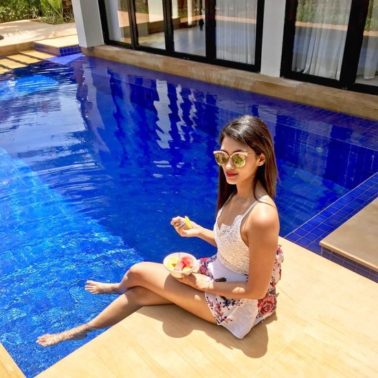 Lady with sunglasses lounging by the pool enjoying a fruit bowl