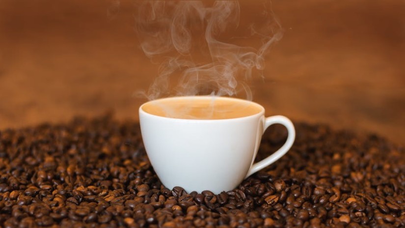 Steaming cup of coffee on a bed of coffee beans.