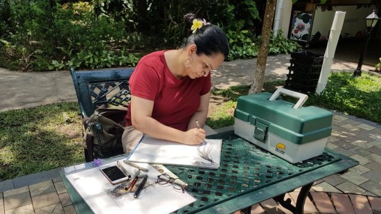 Woman writing on a paper at an outdoor table with tools and a tackle box