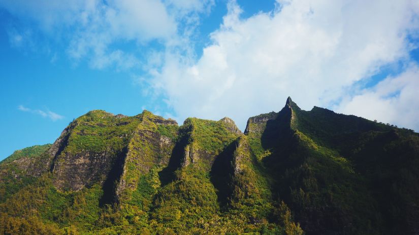 A hill with greenery around and white clouds and blue sky in the background