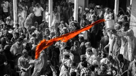 a black and white image of a man throwing colour at devotees at temple