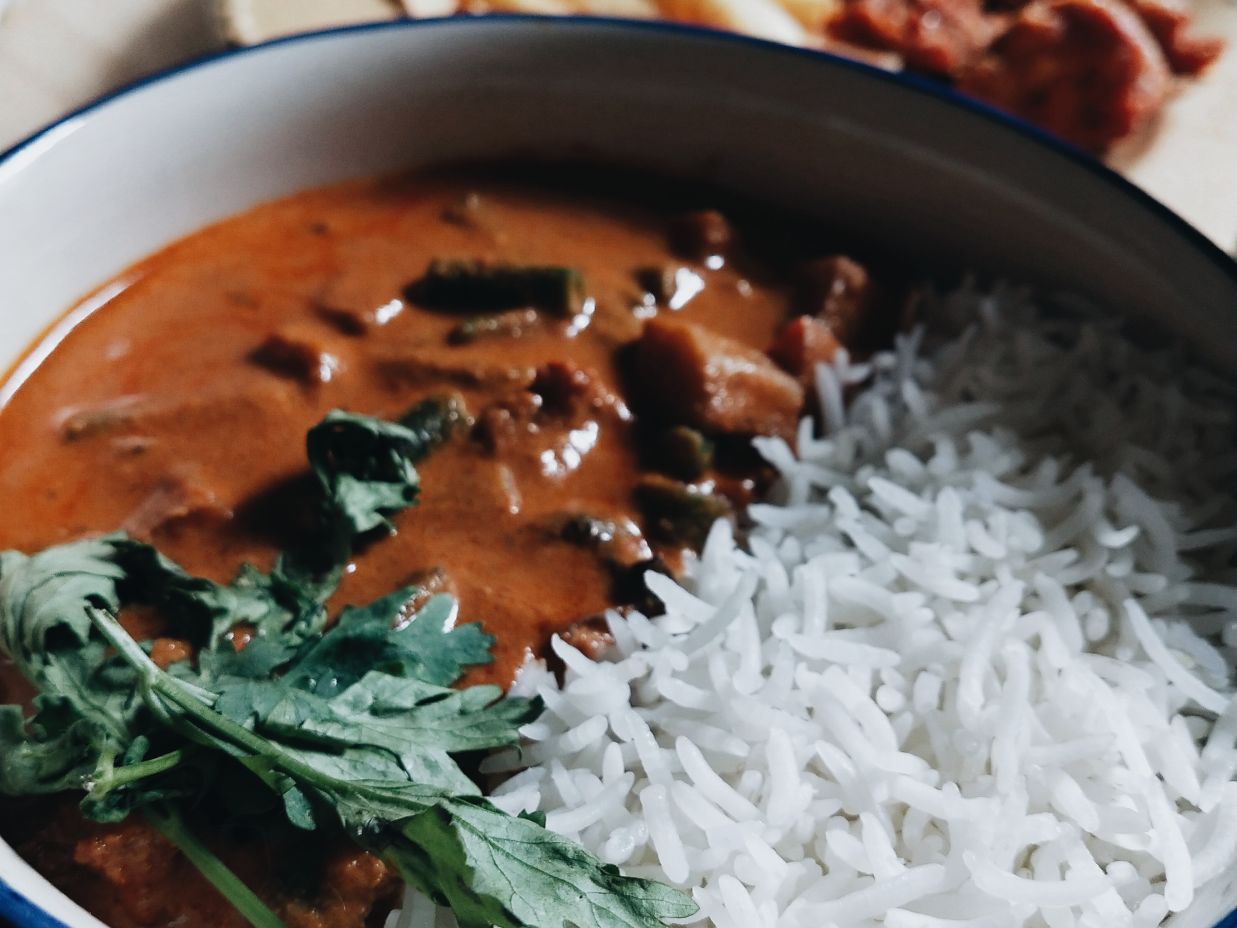 Image of a bowl containing rice and orange coloured curry containing vegetables garnished with corriander leaves