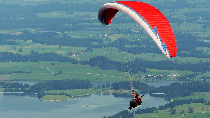 A man paragliding with a scenic view of lush green mountains and lake