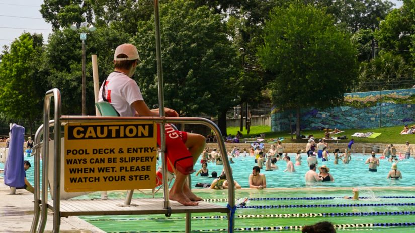 a life guard sitting on top of a stool and a women sitting on the side of a swimming pool