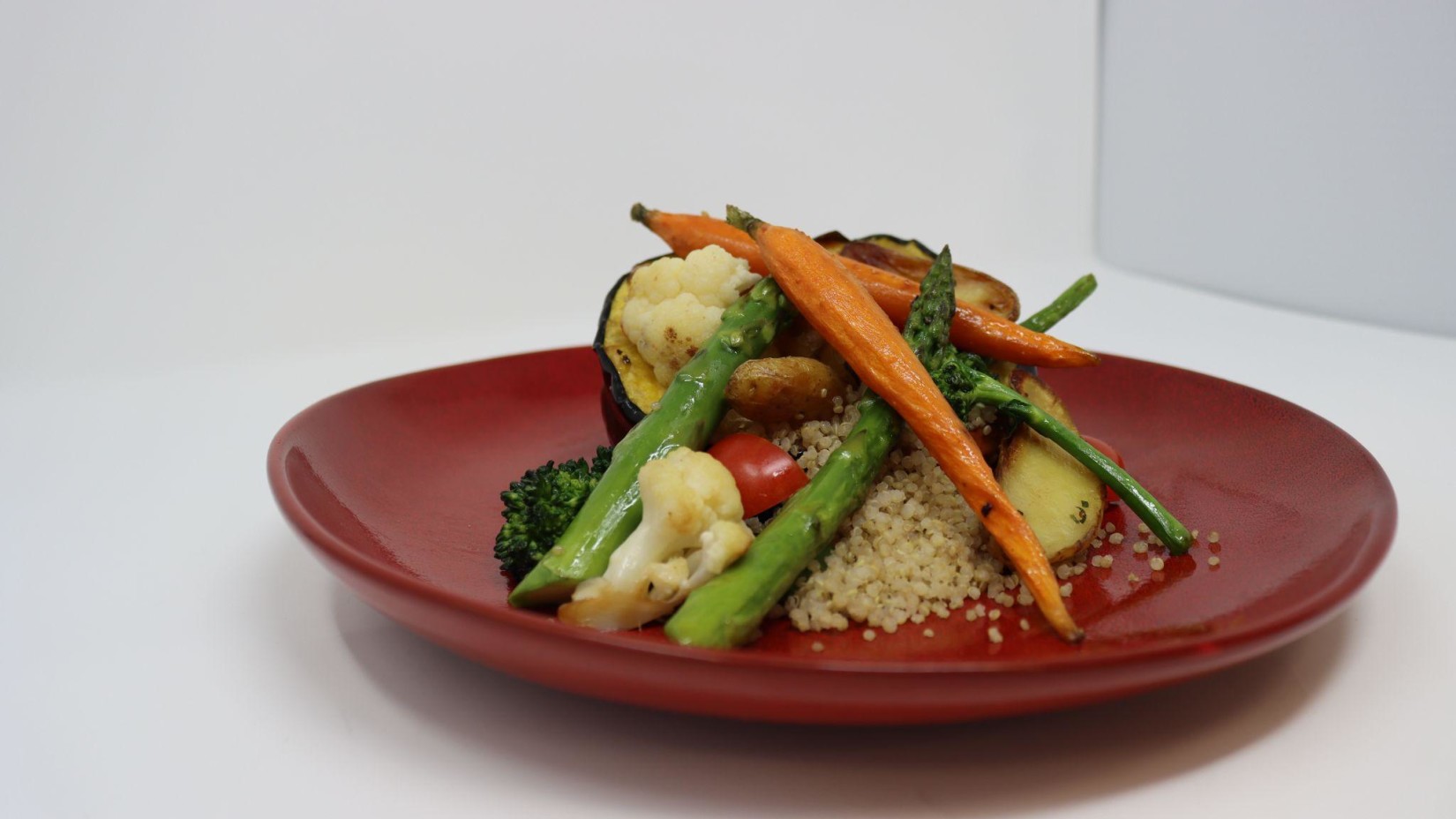 A plate of grilled vegetables and quinoa on a red plate against a white background.