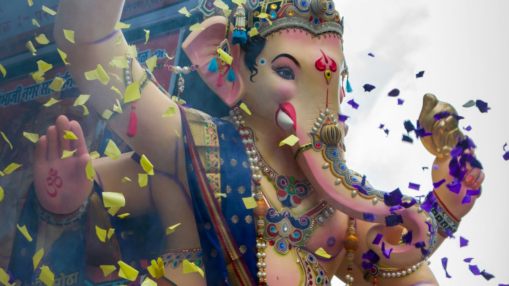 a ganesha's idol kept on a chariot while going for a visarjan with colours being thrown on it