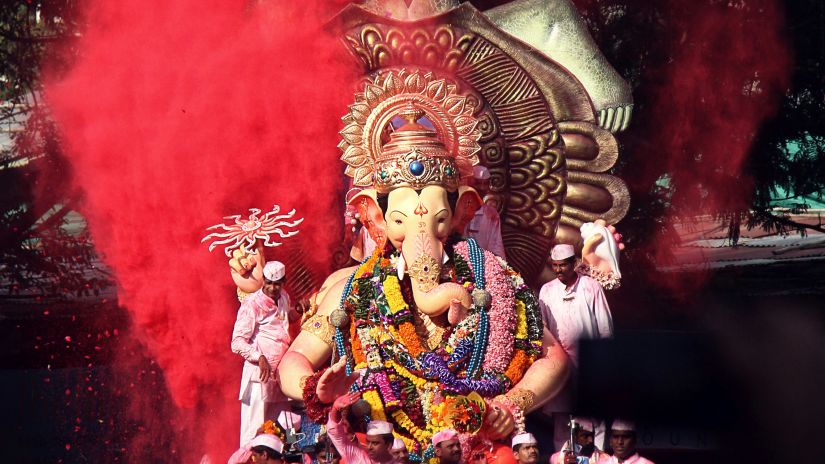 Statue of Lord Ganesha with splash and colour and people during visarjan