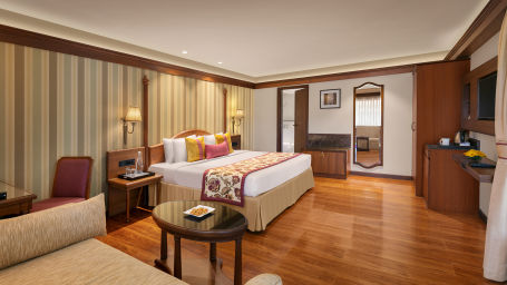 The image shows a luxurious hotel room with a comfortable bed, elegant furniture 