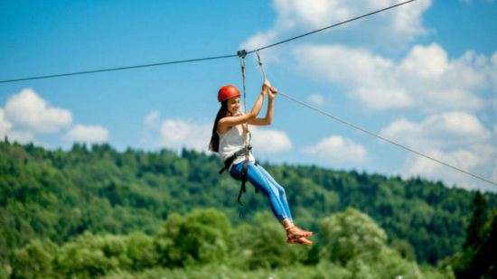 A person on a zipline soars with joy across a scenic landscape, the greenery below providing a beautiful natural backdrop to the adventure.