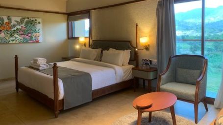 Side view of a double bed with grey bedsheet, an armchair and a small round table at Pride Resort Ambaji