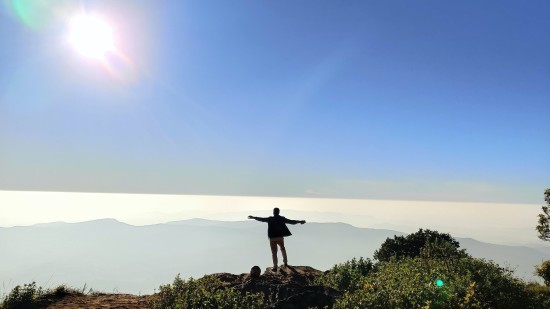 person standing on a cliff with bright sun in the blue sky