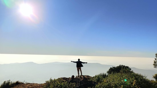 person standing on a cliff with bright sun in the blue sky