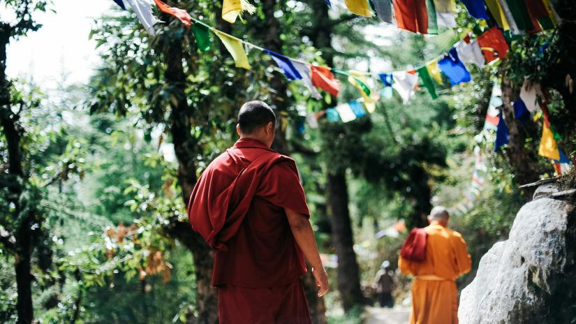 Two monks walking on a hill with prayer flags hanging above it.