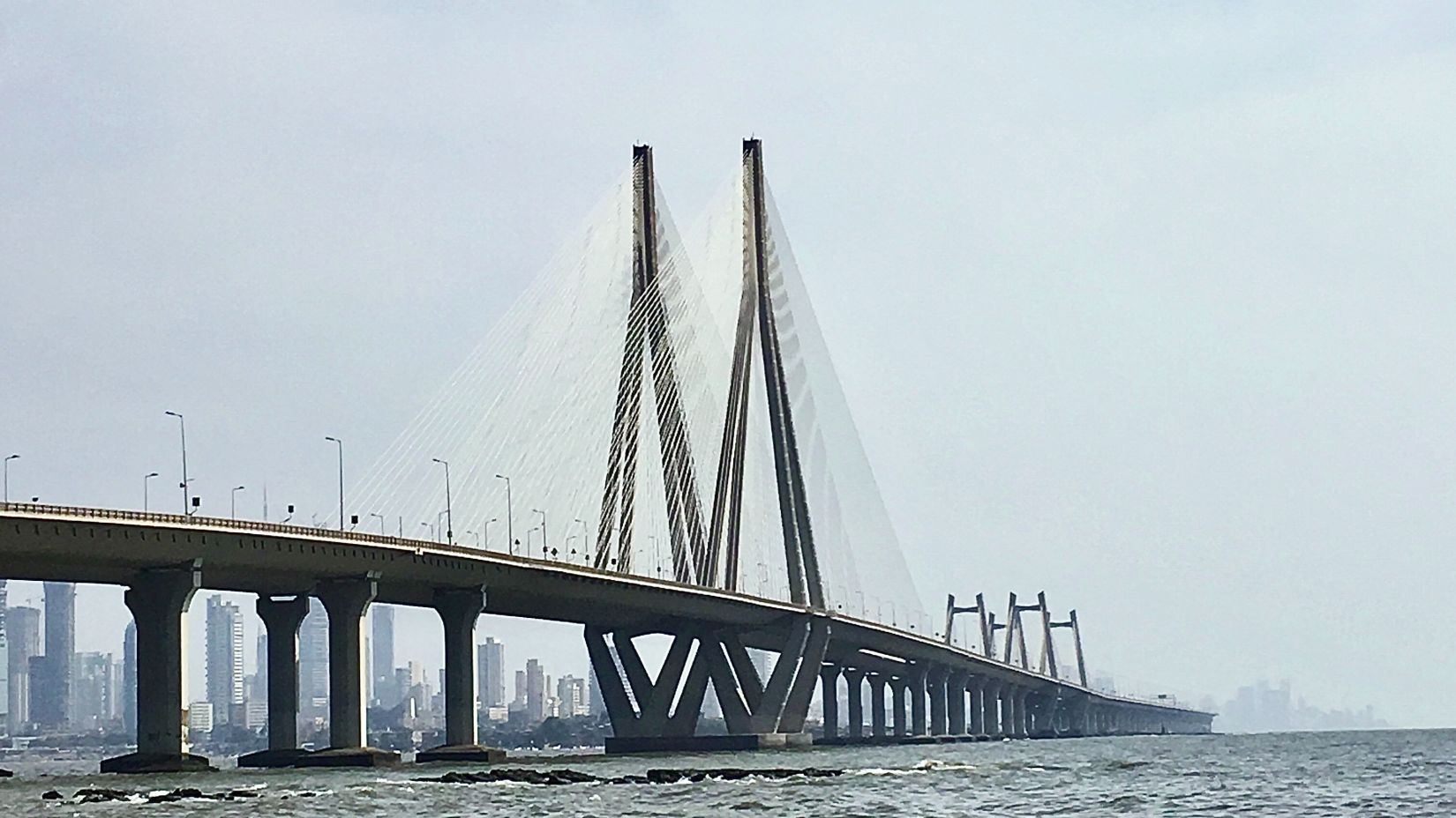 Sea waves hitting the rocks as the Worli sea link is visible at the distance