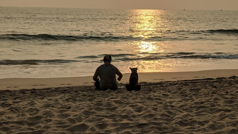 a man and a dog sitting on the sand and watching the sunset at Agonda Beach in goa