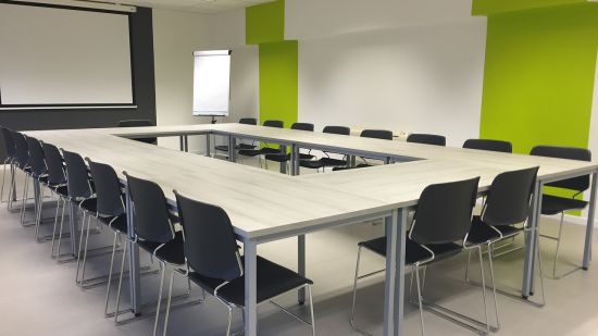 A seating area with multiple chairs a big table and a projector