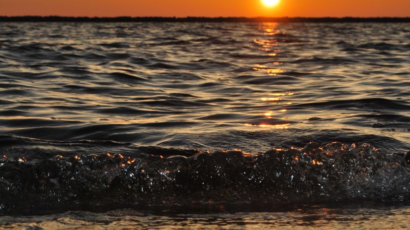 A view from the beach of the overlapping waves and the sun setting in the background