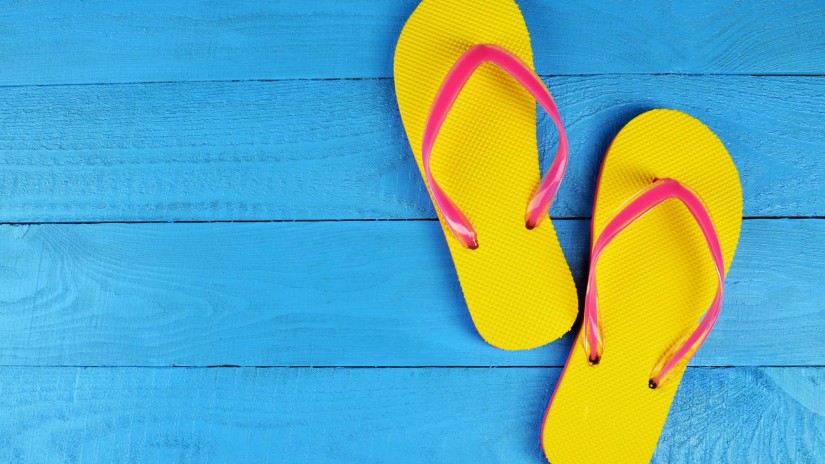 Pair of bright yellow flip flops kept on a blue deck