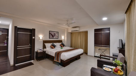 Another view of a superior room with a large bed, two lamps hanging above it, two comfortable chairs and an attached bathroom - Click Hotel Yuvraj, Surat