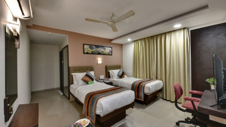 A deluxe room with twin beads, a work desk and a revolving chair - Click Hotel Yuvraj, Surat