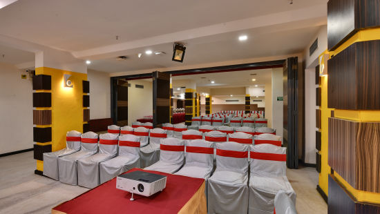 A banquet hall with grey and red covered chairs and a projector placed on a table - Click Hotel Yuvraj, Surat