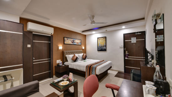 A deluxe room with a large bed, an attached bathroom and a ceiling fan attached above it - Click Hotel Yuvraj, Surat
