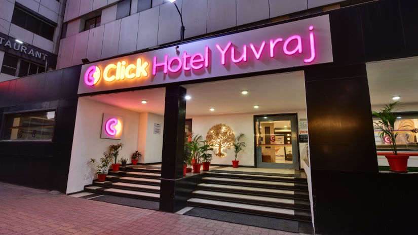 Frontal view of Click Hotel Yuvraj entrance with neon signs and decorative plants - Click Hotel Yuvraj, Surat