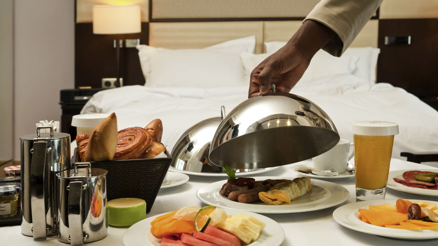 a person opening the cloche to relish breakfast that is served on bed