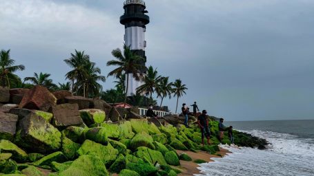 A lighthouse on a beach with greenery on a cloudy day