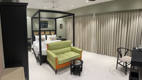 A king bed, a sofa, a small table and a study chair at the end of the room inside luxury room - Hotel Mumbai House, Malad