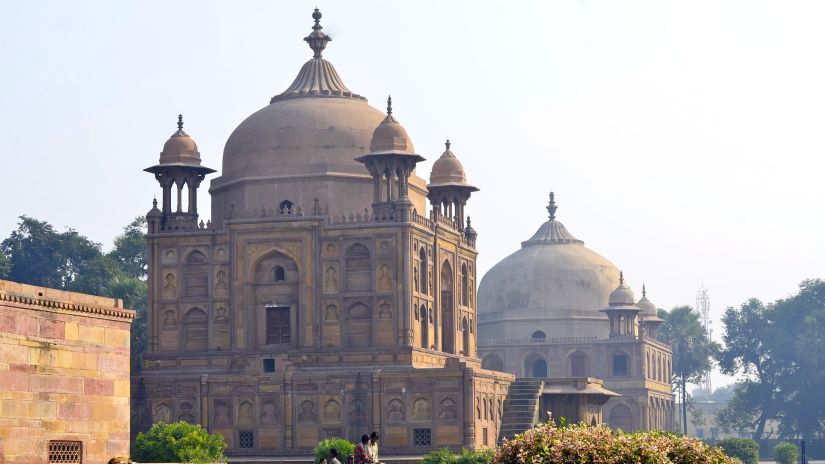 A domed sandstone mausoleum in a garden setting under a clear sky.