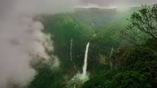 an aerial view of a hill station with a waterfall and clouds floating by