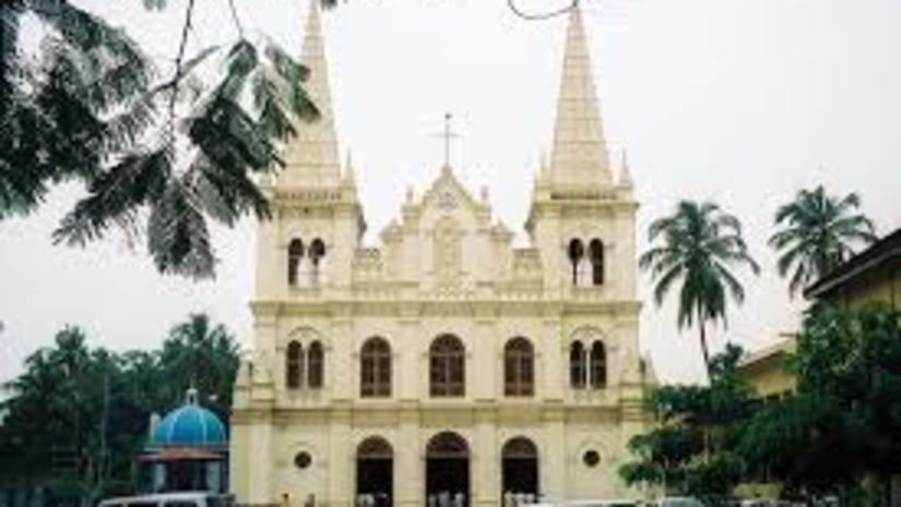 The Tower House - Santa Cruz Basilica Church in Kochi with coconut trees around and cars parked in front 