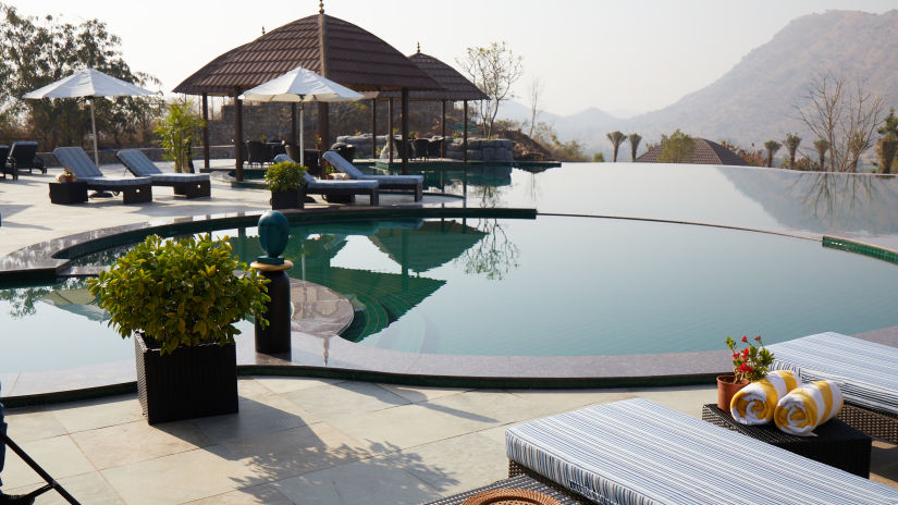 The Infinity Pool with beach chairs and gazebos nearby - Staycation in Udaipur