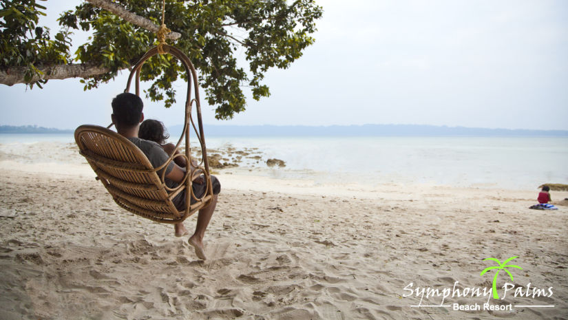 A person with a child on a swing resting at the beach