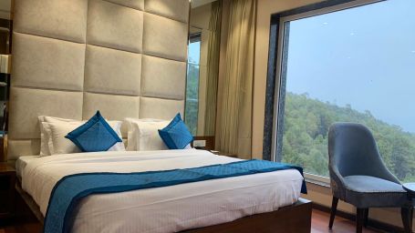 Side view of Deluxe room with plush bed and bedside tables, seating area with coffee table - Mastiff Hotel, Dalhousie