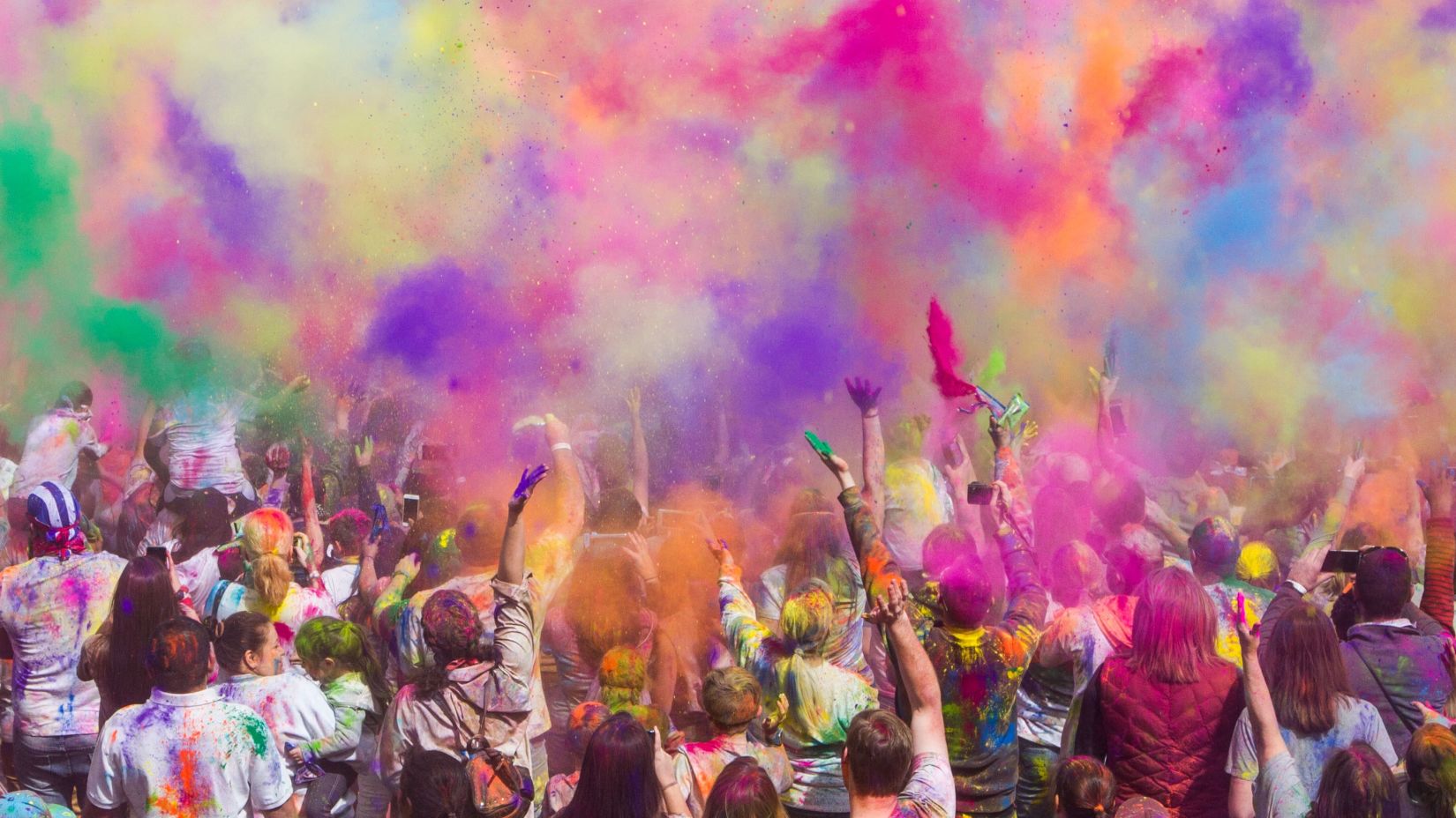 People gathered together and throwing coloured gulal in the air