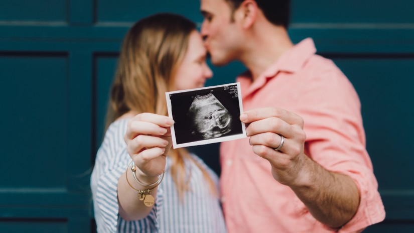 a couple posing together with a pregnancy ultrasound picture in their hand