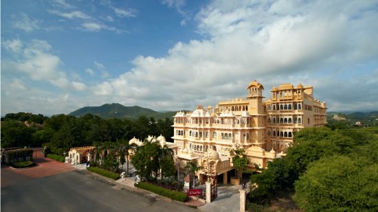 Facade image of Chunda Palace next to many trees and blue sky covered in white clouds - Chunda Hotels