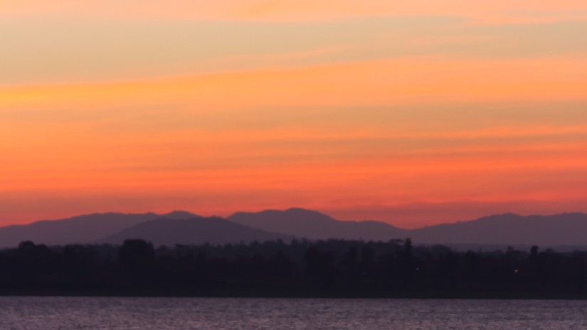 a boat travelling on a waterbody with the sky having different hues after a sunset