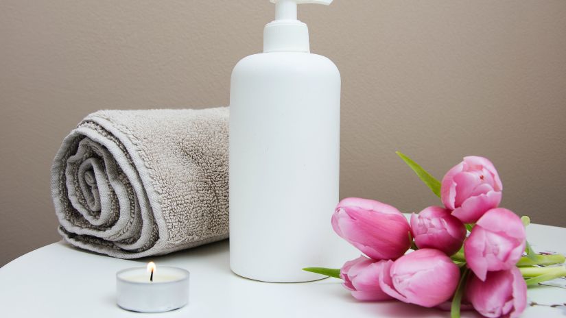 a bottle of lotion placed on a table along with a towel, candle and flower