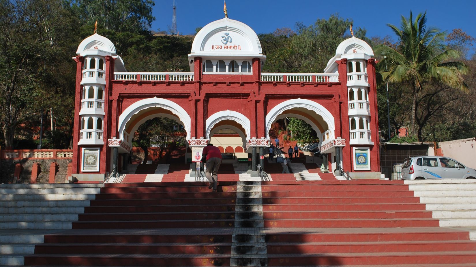 A red temple surrounded by lush green trees -Fort JadhavGADH 