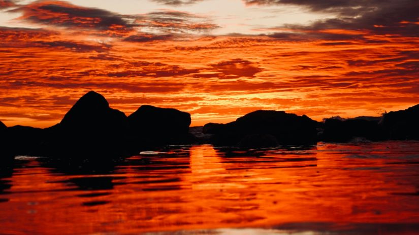 A view of a beach after a sunset with different hues of red and orange in the sky